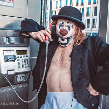 Anatoli Akerman holding a red telephone receiver beside a street payphone. Photo: Dmitry Shakhin.